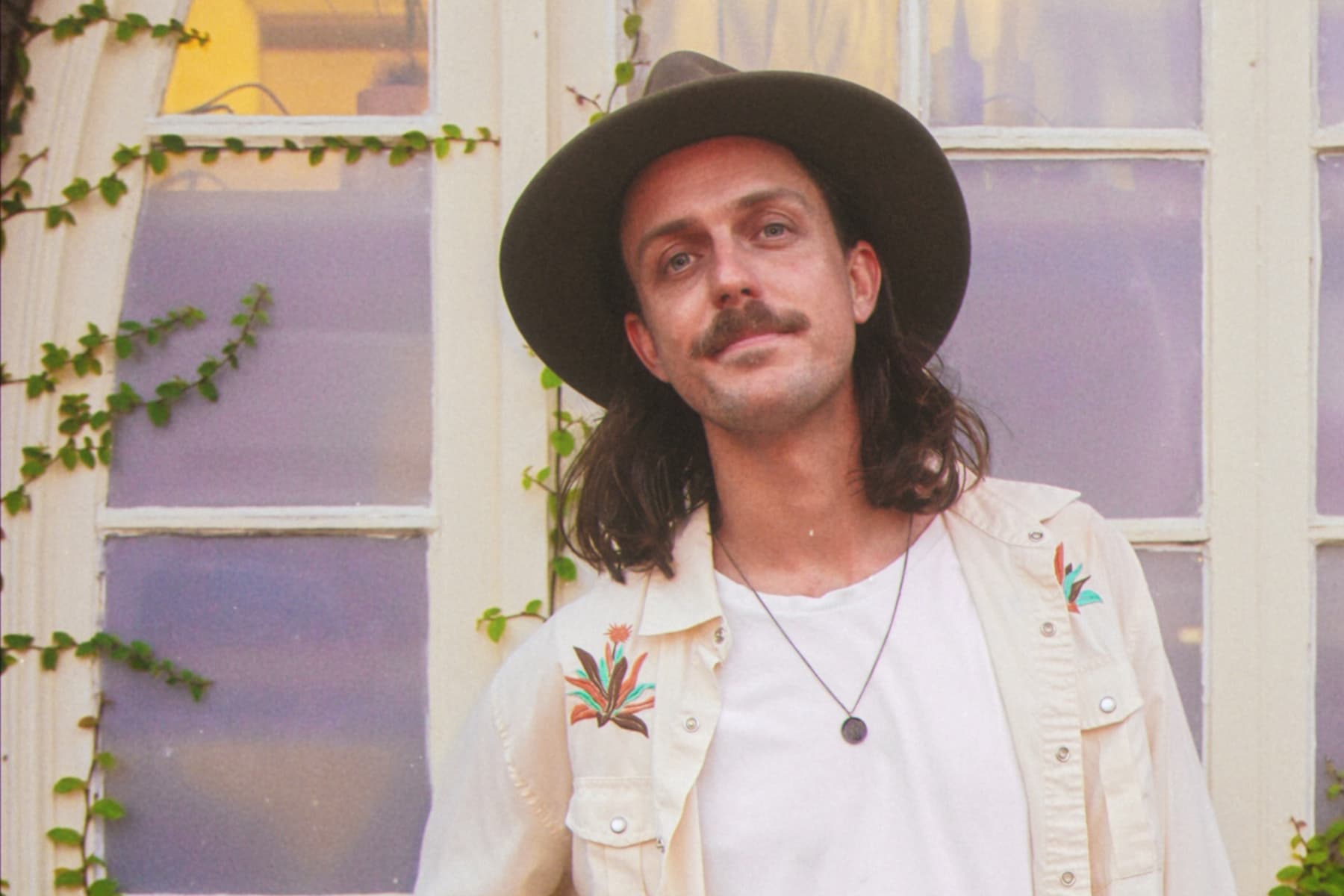 Benjo in embroidered shirt by a window with ivy